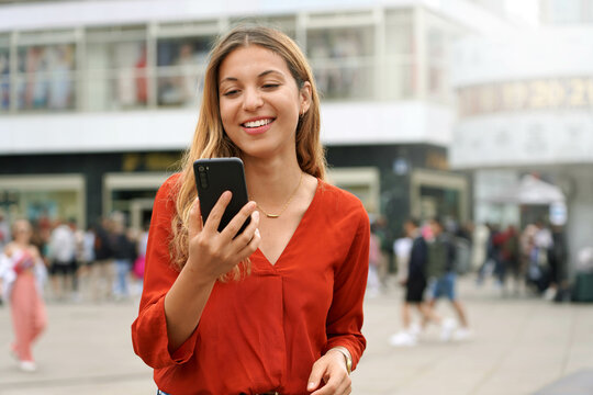 Attractive young woman holding a mobile phone watching videos on app in Berlin city square, Germany