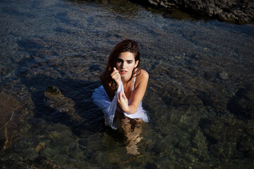 Alluring young lady sitting in sea water and looking at camera