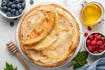 Stack of French crepes or traditional Russian blini on white plate on light background. Thin...