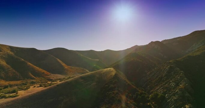 Amazing mountainous territory with no trees growing on. Drone rising over the mountains in the rays of bright sun.