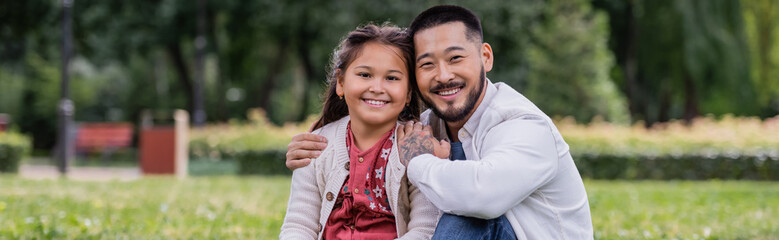 Asian parent hugging smiling preteen kid in park, banner.