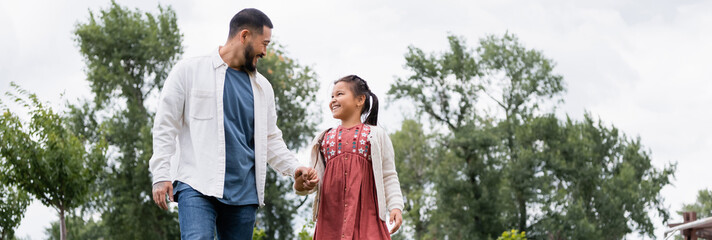 Cheerful asian father and daughter holding hands in park, banner.