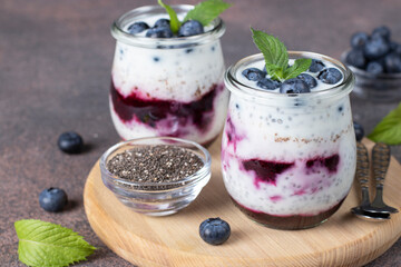 Chia pudding with blueberry and jam in two glass jars on wooden board on brown background