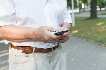 A mobile phone in the large hands of an elderly man in a white shirt on a walk in the park