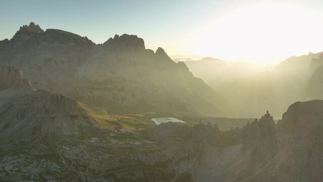 View from above, stunning aerial view of a mountain range during a beautiful sunrise with a mountain hut in the distance. Tre Cime di Lavaredo, Dolomites, Italy.