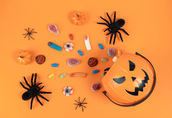 Halloween Jack o Lantern basket with candies and spiders, top view on a orange background