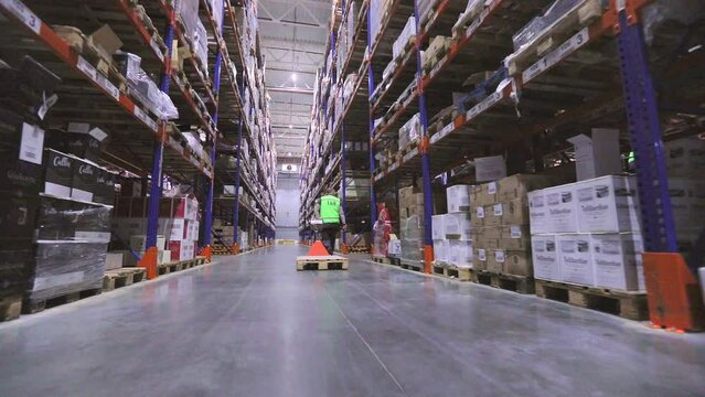 A worker carries goods on a forklift. A man in a large warehouse is carrying a hydraulic pallet truck rear view. Warehouse worker. Large modern warehouse