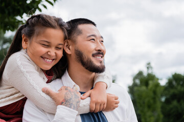 Cheerful asian daughter hugging tattooed father in park.