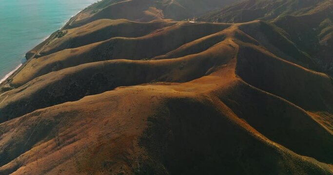 Amazingly beautiful smooth brown mountains with no vegetation at the waterfront of the sea. Sunlit hills from aerial perspective.