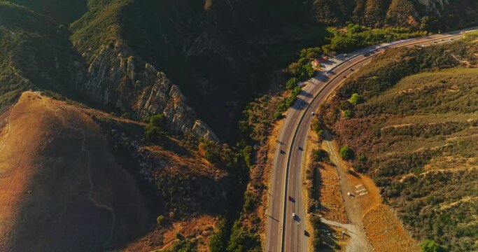 Freeway in the mountainous locality on sunny bright day. Descending drone footage over the road with moving cars. Aerial view.