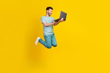 Full length photo of impressed excited man dressed striped t-shirt blue pants jumping look on laptop isolated on yellow color background