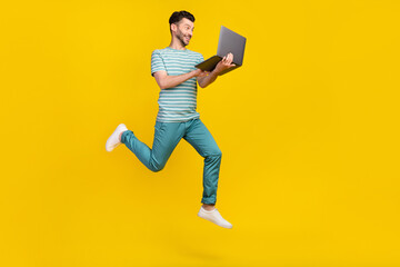 Profile full length photo of impressed guy run with laptop wear t-shirt jeans sneakers isolated on yellow color background