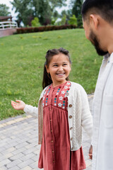 Smiling asian child looking at blurred father in park.