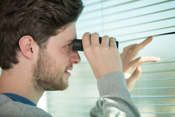 young man standing looking through a glass window with binoculars