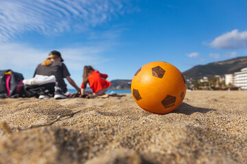 Obraz premium The concept of relaxing on the beach with children. Beach games. Vacation and weekend. Close-up of a ball on the sand against the background of people resting