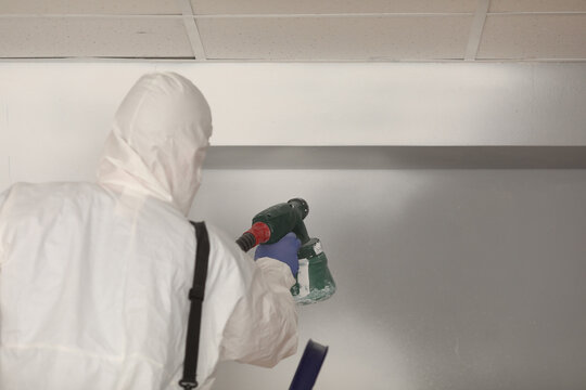 Worker paints wall white with spray gun