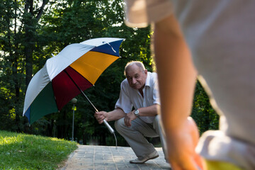 Grandson and grandfather to move out in the park under a bright umbrella at sunset. A pensioner and a little boy spend their free time on weekends together.