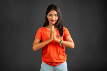 Beautiful Indian girl with welcome expression or inviting or greeting Namaste on a grey background.