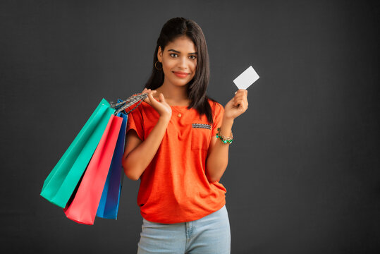 Beautiful young girl holding and posing with shopping bags and credit or debit card on a grey background