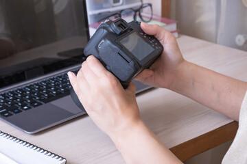 Studying online photography lessons. Female hands holding SLR camera at desktop with laptop