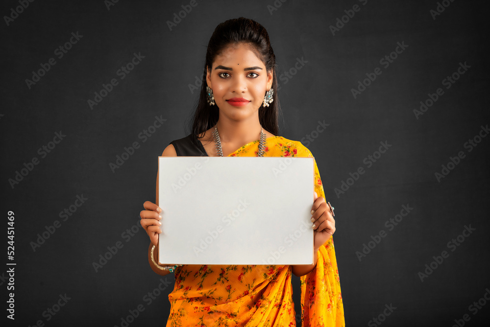 Sticker a young girl or businesswoman wearing a saree and holding a signboard in her hands on a gray backgro