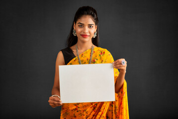 A young girl or businesswoman wearing a saree and holding a signboard in her hands on a gray...
