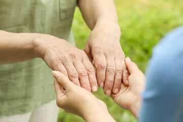 Elderly woman and female caregiver holding hands outdoors, closeup