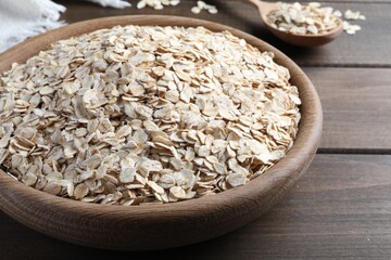 Raw oatmeal in bowl on wooden table, closeup