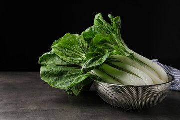 Fresh green pak choy cabbages with water drops in sieve on grey table - obrazy, fototapety, plakaty