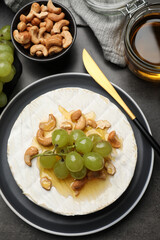Brie cheese served with grape, cashew nuts and honey on dark grey table, flat lay