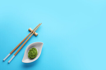 Bowl with swirl of wasabi paste and chopsticks on light blue background, flat lay. Space for text