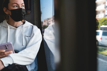 A yong woman in a protective medical mask sits near the window on the bus. Social distance and...
