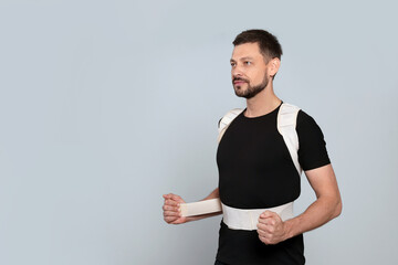 Handsome man with orthopedic corset on grey background, space for text