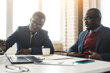 Two African American business partners are working on a laptop studying stock market charts and...