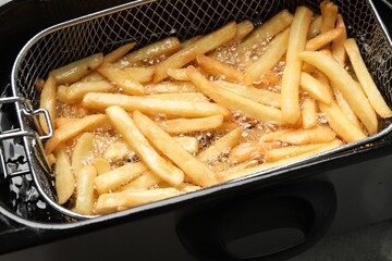 Cooking delicious french fries in hot oil, closeup