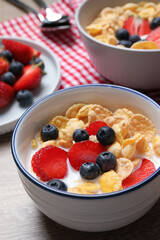 Delicious crispy cornflakes with milk and fresh berries on wooden table, closeup