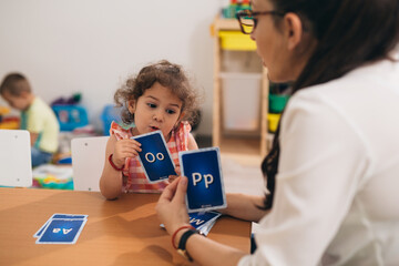 teacher teaching child to correct pronouncing the words at child daycare - obrazy, fototapety, plakaty