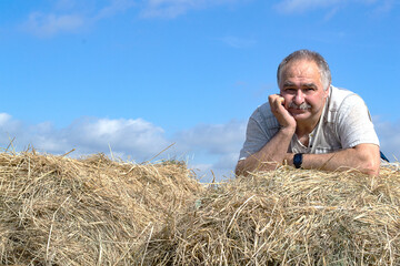 Naklejka na ściany i meble A contented elderly man with a mustache lies on a haystack with his chin resting on his hand