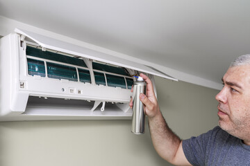 man cleans the air conditioning with antibacterial spray