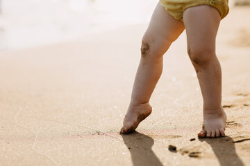 Closeup of baby feet walking on tiptoes on beach sand, barefoot.