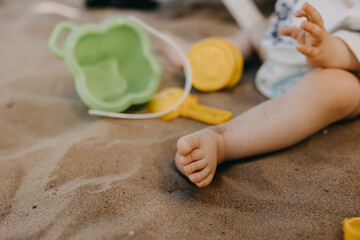 Closeup of a baby foot on sand. Child playing with colorful toys on the beach