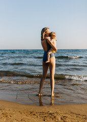 Woman holding little child in arms, standing at a seashore.