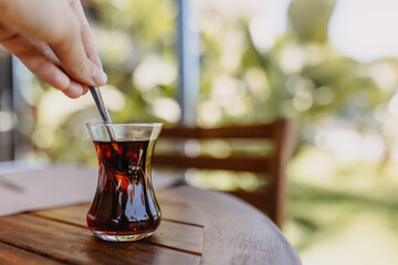 Closeup of a human hand steering black hot turkish tea in a small glass.