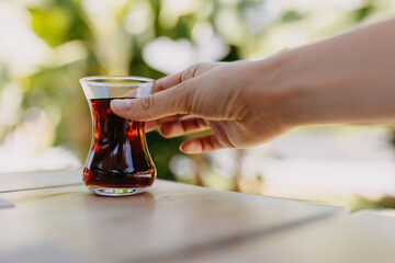 Hand holding a small glass with turkish tea, outdoors.