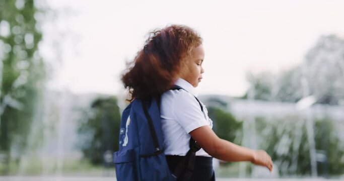 The schoolgirl goes to school for a lesson. African american teenager with a backpack joyfully runs early in the morning in the park to study, concept child studying at school