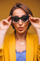 Portrait of woman in yellow suit wearing black and white sunglasses isolated in studio