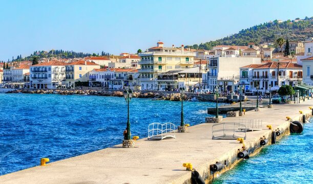 A view of the port skyline of the beautiful Greek Island, Spetses, the pier leading to the city and some of the local architecture.

