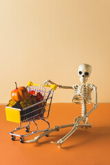 Skeleton With Shopping Cart Trolley with Halloween Sweets Halloween Concept Orange Background