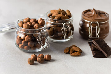 Glass Jar with Chocolate nut Cream and Raw Nuts on a Concrete Background and Pieces of Chocolate Horizontal