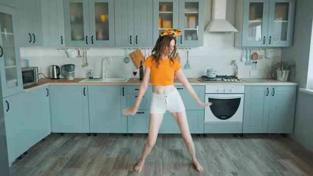 A beautiful woman in white shorts is relaxing at home, dancing in the kitchen